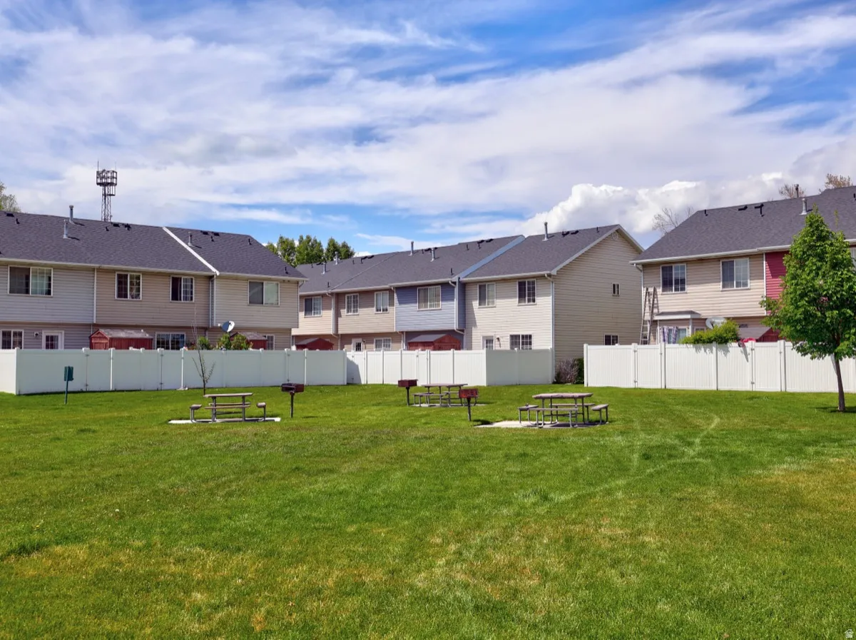 Expansive green space featuring picnic tables and barbecue grills, bordered by a white vinyl privacy fence