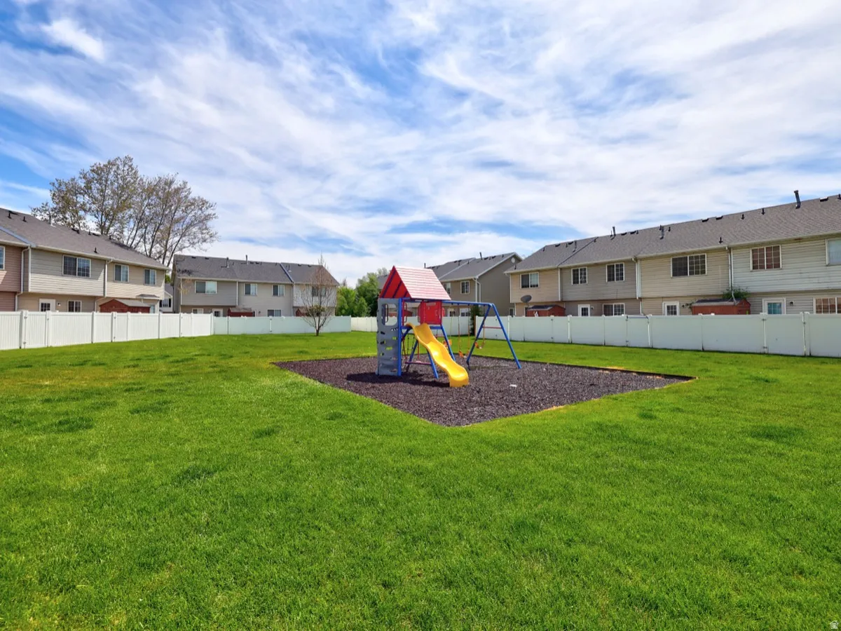 Expansive common green space with a dedicated play structure featuring a slide and swings, surrounded by a white privacy fence