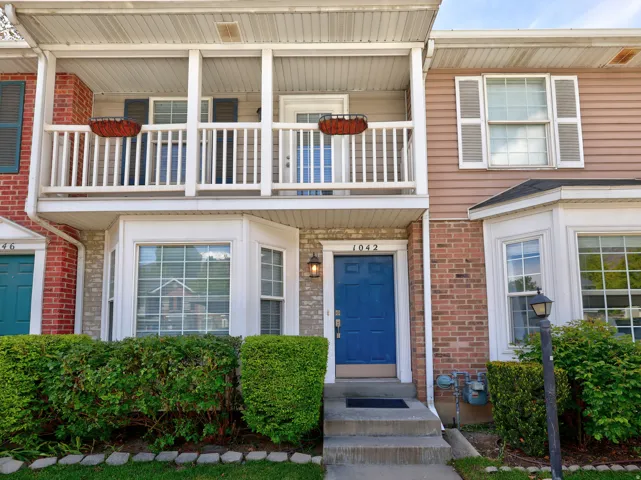 Townhome exterior featuring a prominent blue front door, a second-story balcony with white railing, a bay window on the main level, and brick and siding facade elements