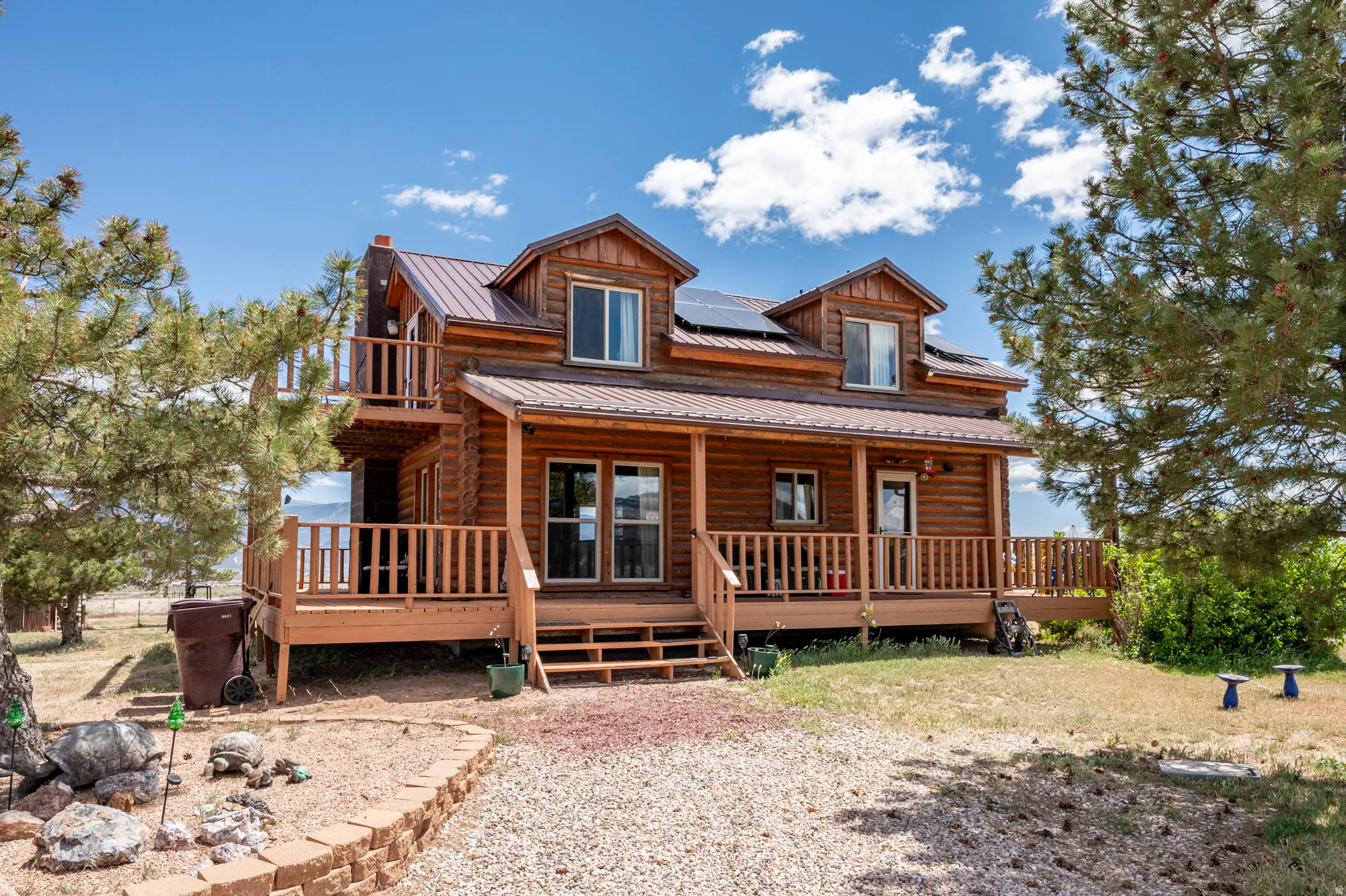Log cabin exterior featuring a covered porch, an upper-level balcony, dormer windows, and a metal roof