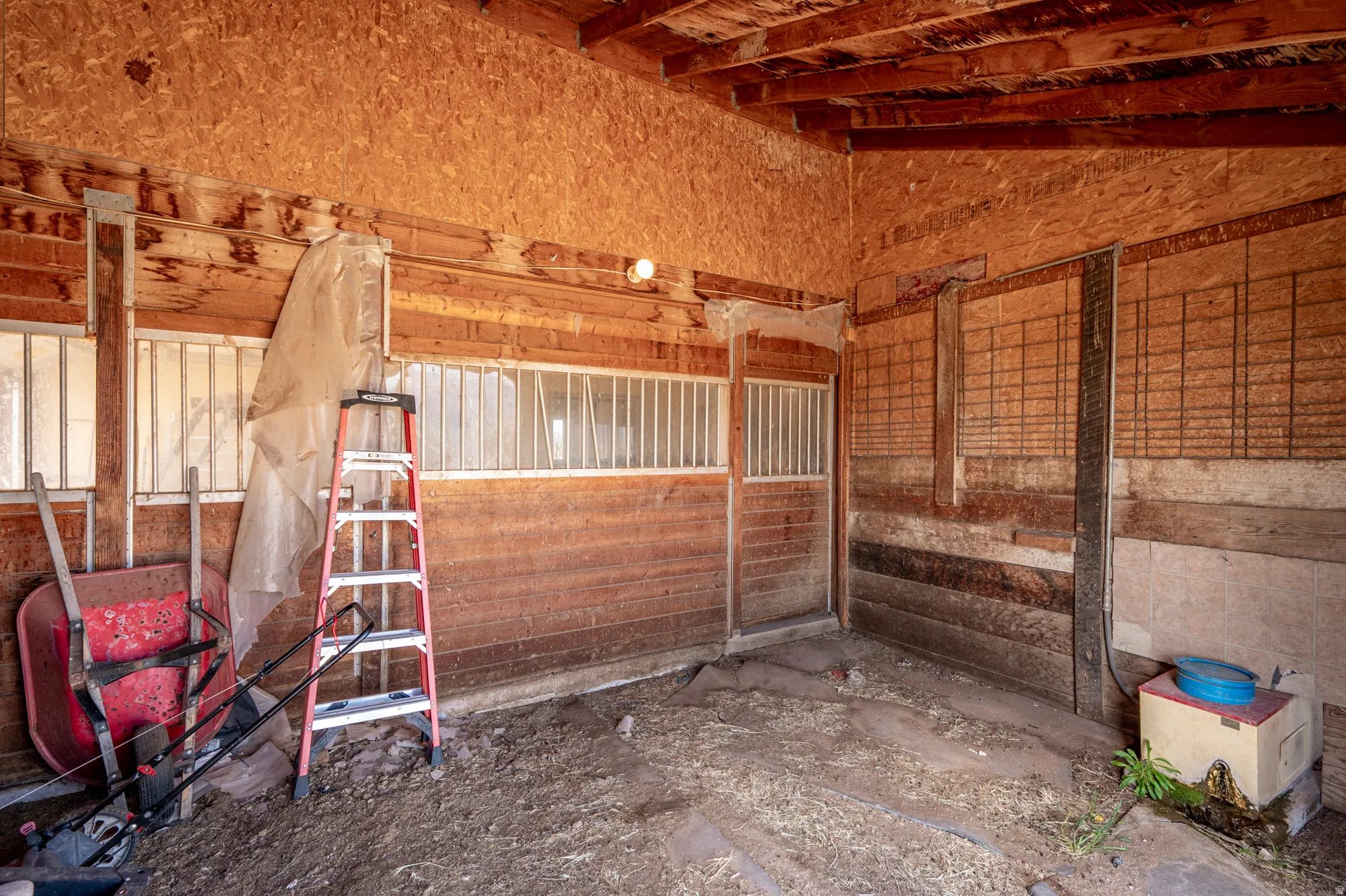 Barn interior featuring wood plank walls, exposed wood beam ceiling, and individual stalls with metal grate windows