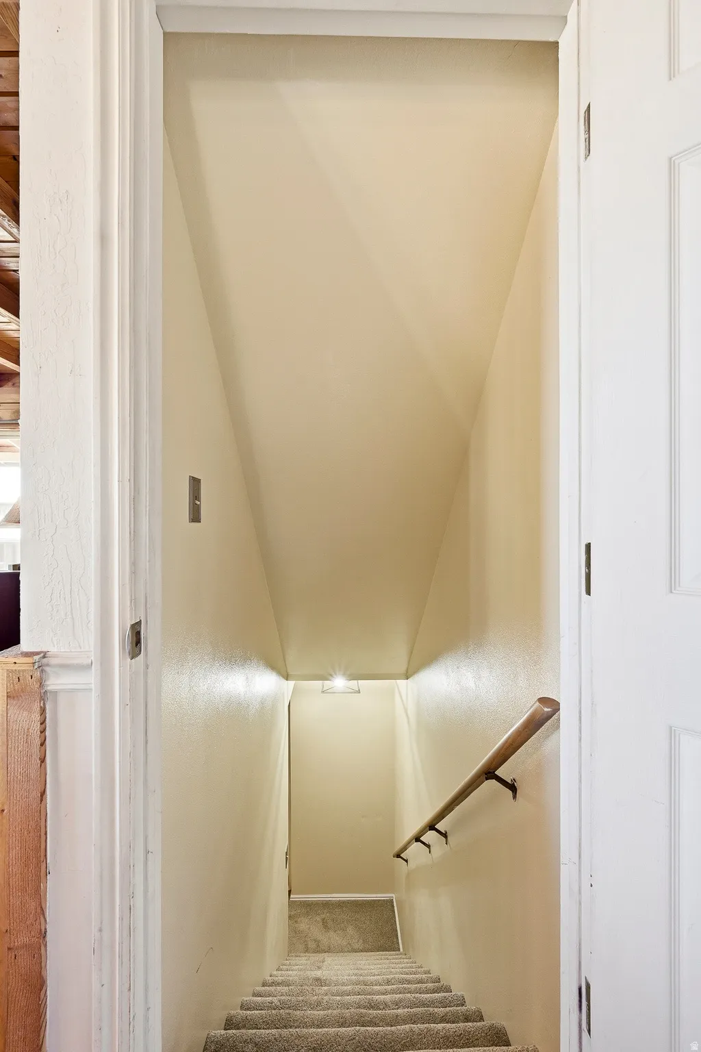 Carpeted staircase with a wood handrail, recessed wall lighting, and painted walls