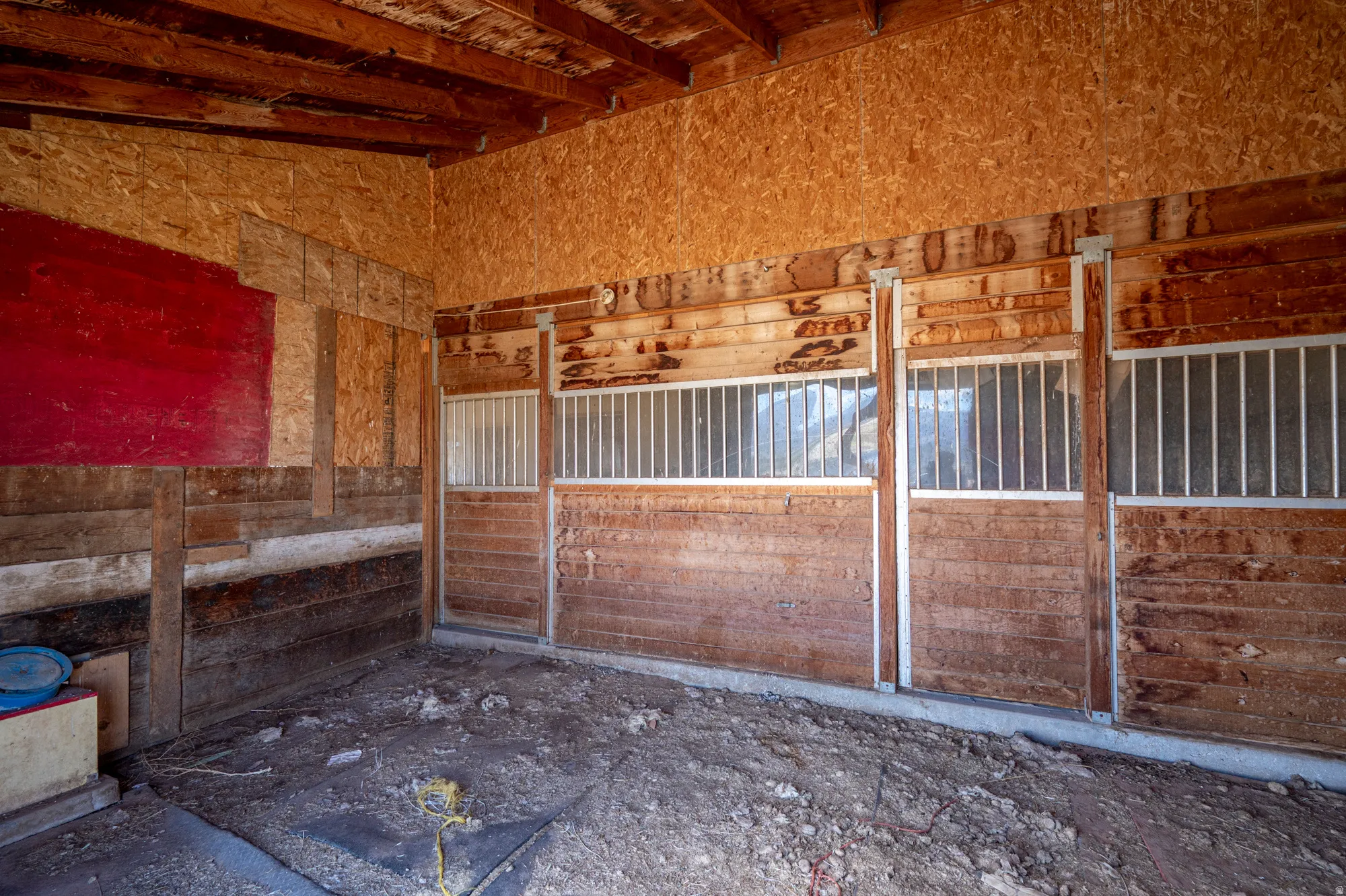 Interior barn stalls featuring wood paneling, metal grate windows, and exposed wood ceiling beams