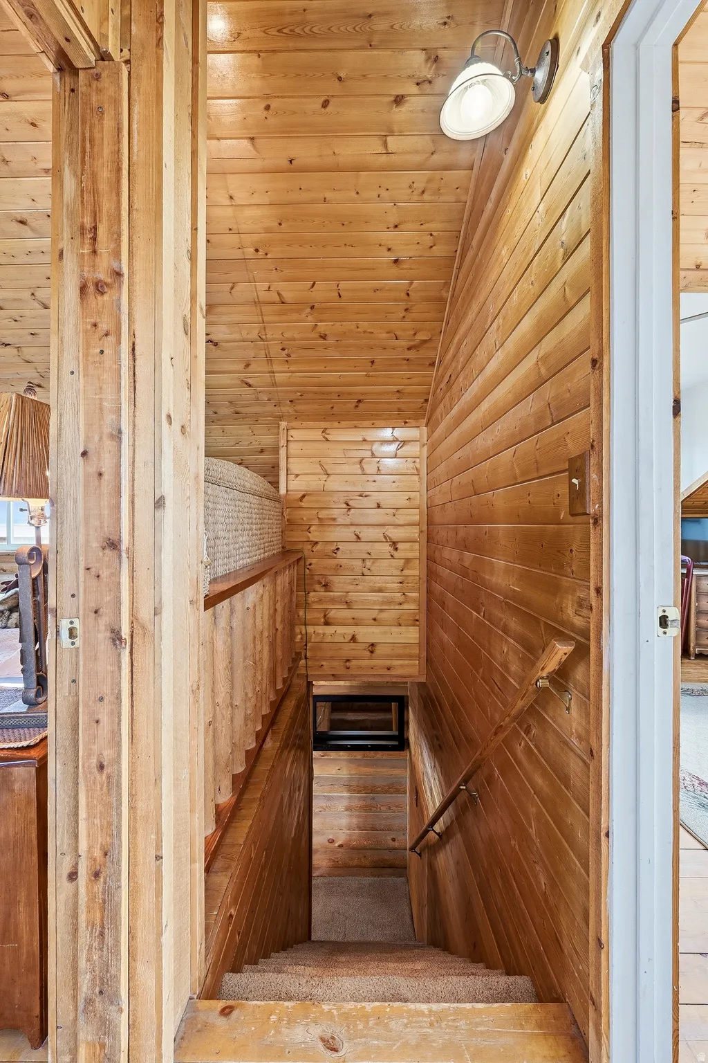 Wood-paneled staircase featuring carpeted treads, wood handrails, and a wall-mounted light fixture