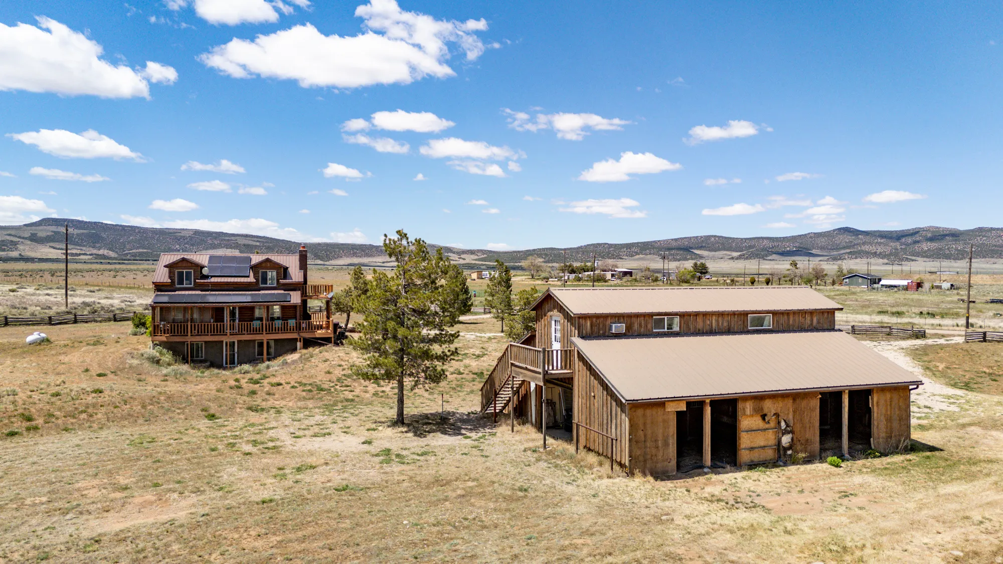 Rustic wood-sided barn with a metal roof, featuring multiple open stalls and an exterior staircase accessing an upper level