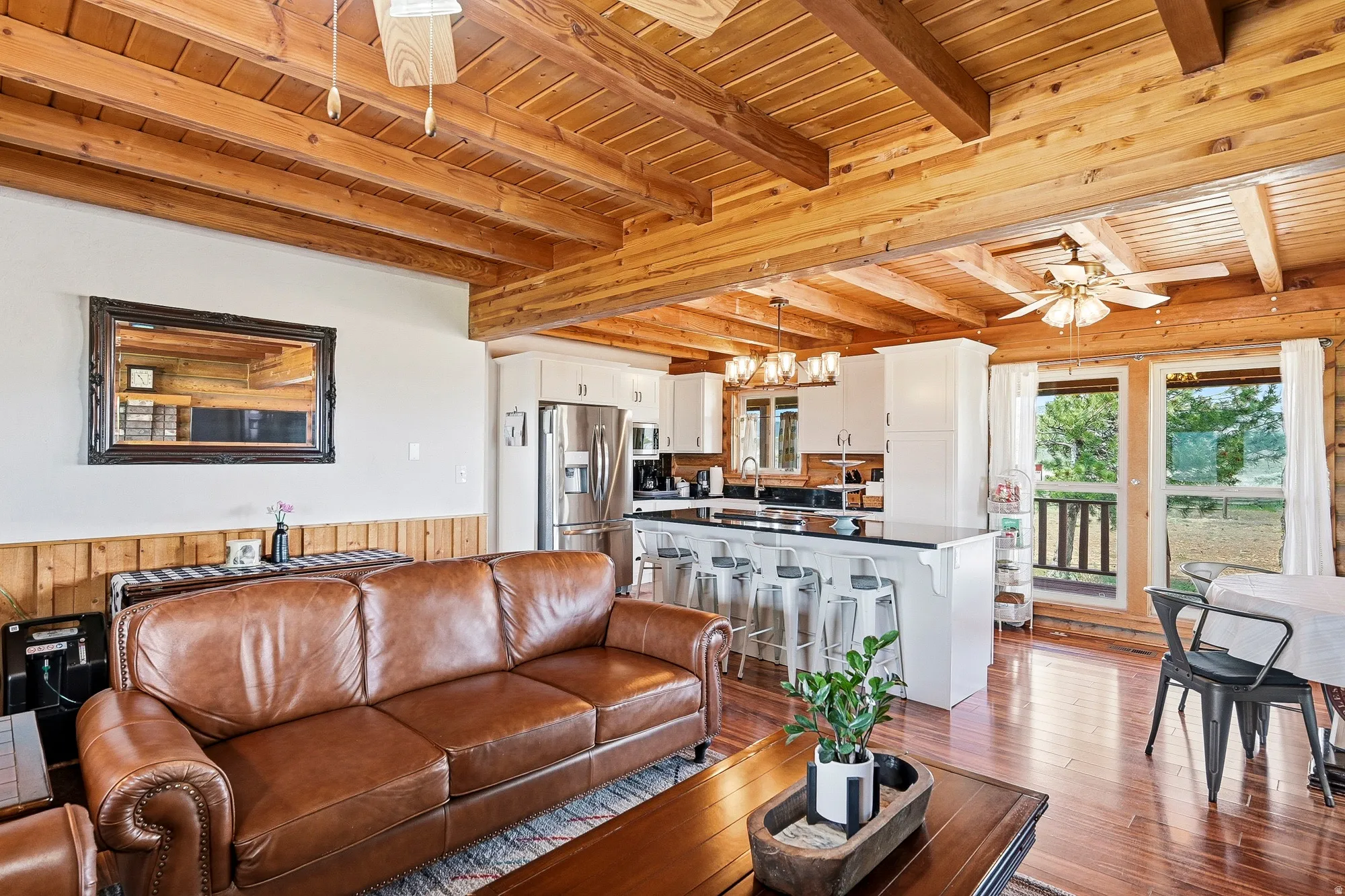 Open-concept living space featuring wood-finish flooring, exposed wood beam ceilings, and white wainscoting