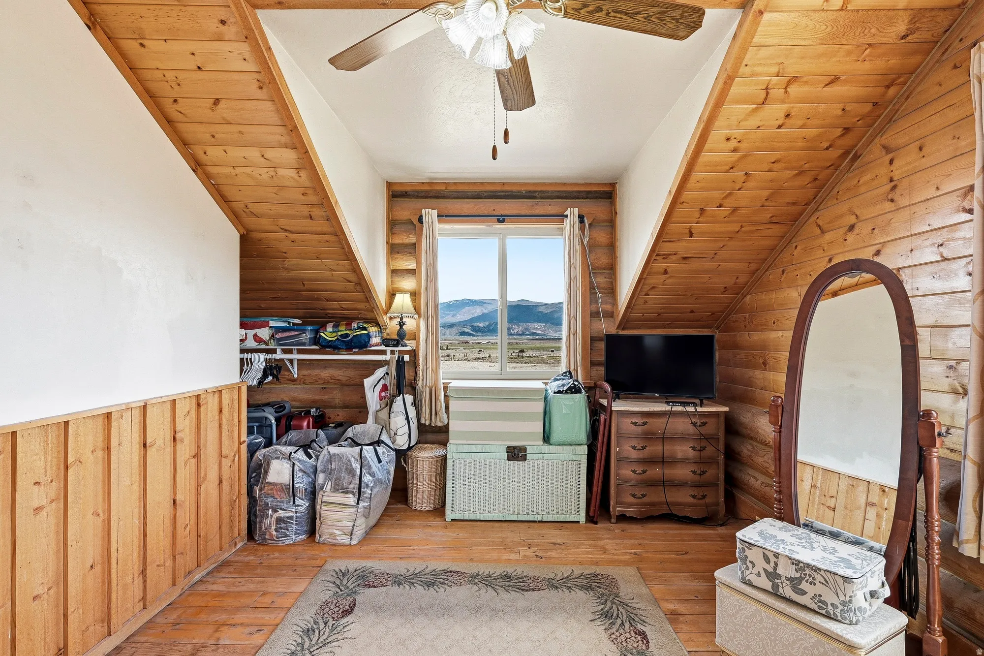 Attic space featuring wood-finish flooring, wood-paneled walls, a sloped ceiling with wood beams, and a central ceiling fan