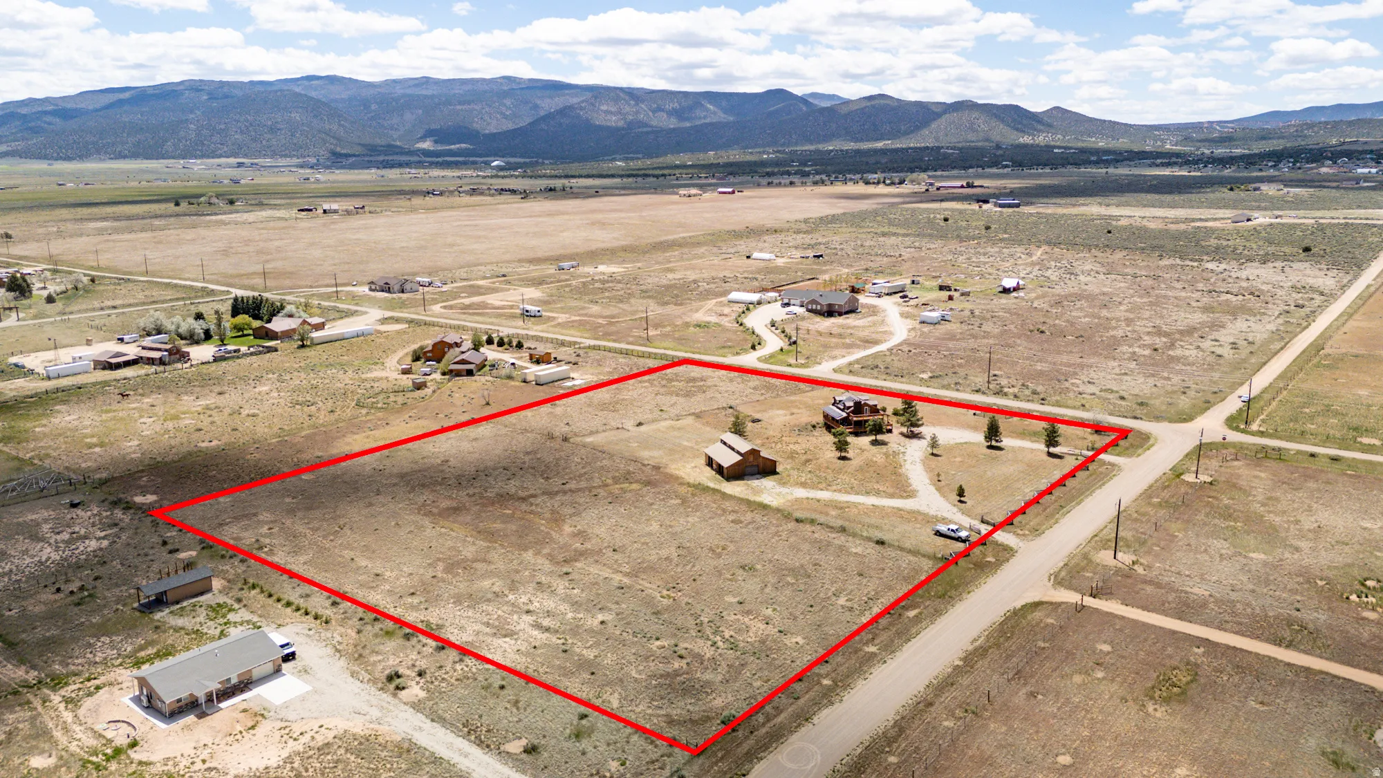 Expansive land parcel with a visible red boundary line, featuring a primary residence with a brown exterior and a detached barn-style structure