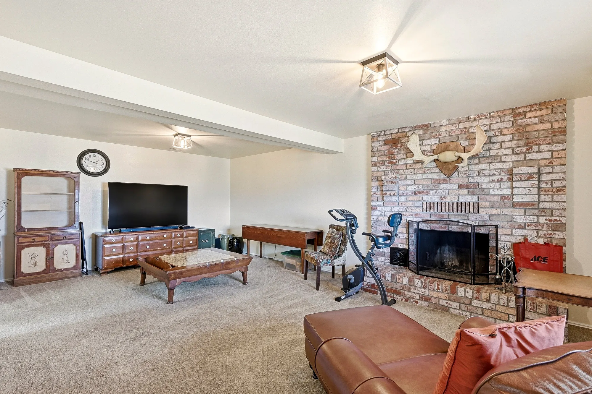 Spacious room featuring a brick fireplace with a black metal screen, neutral-toned carpeting, recessed ceiling lighting, and a prominent white ceiling beam
