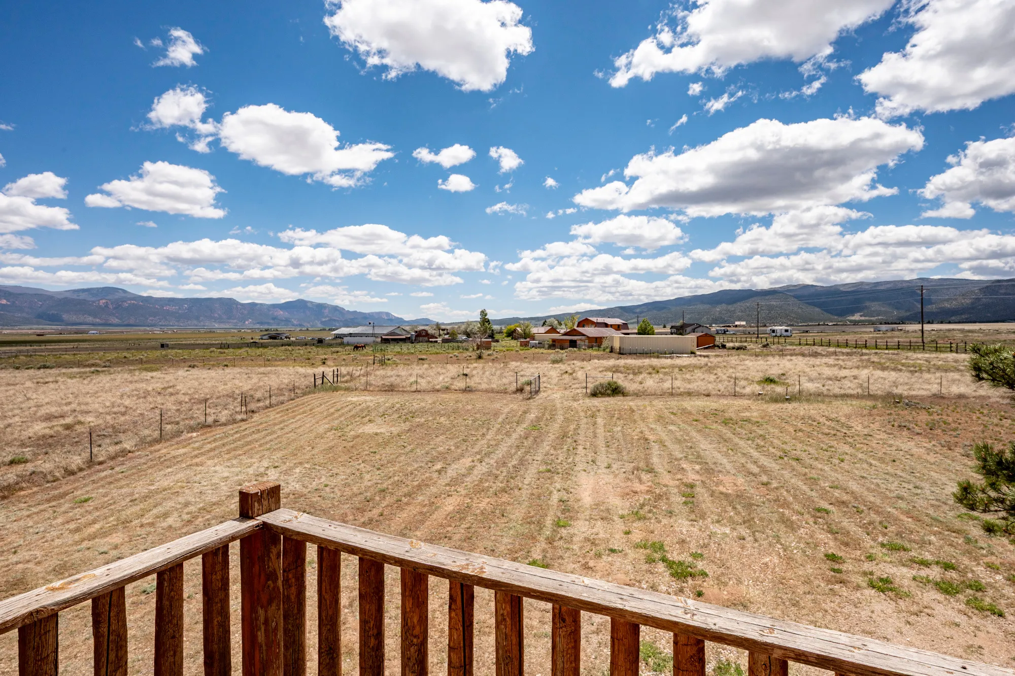 Expansive rural landscape featuring distant mountains and a blue sky with scattered clouds