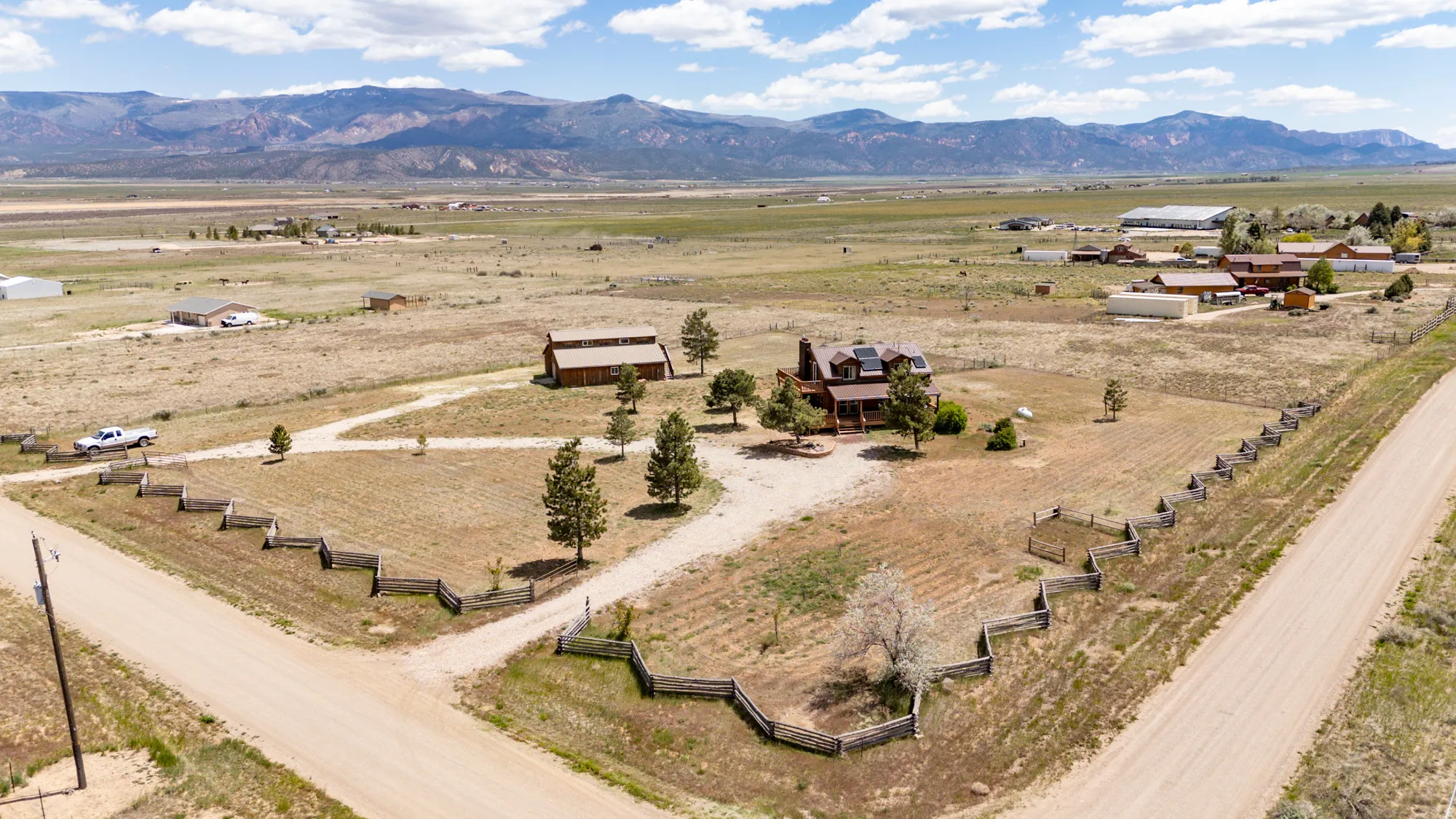 Expansive property featuring a multi-level residence with exterior decks, a separate barn structure, mature trees, and split-rail fencing
