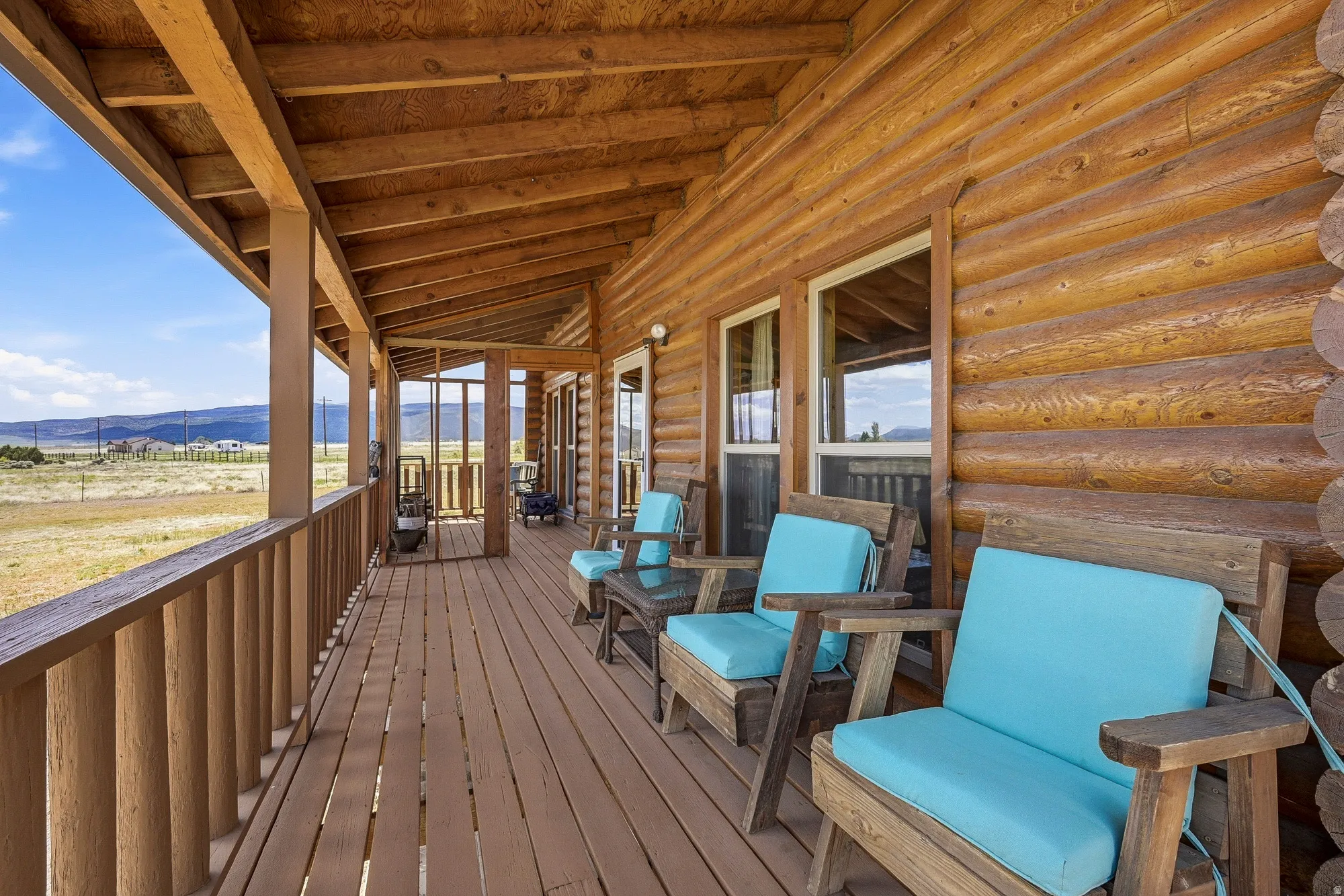 Expansive covered porch featuring a log cabin exterior, exposed wood beam ceiling, wood plank flooring, and a spindle railing