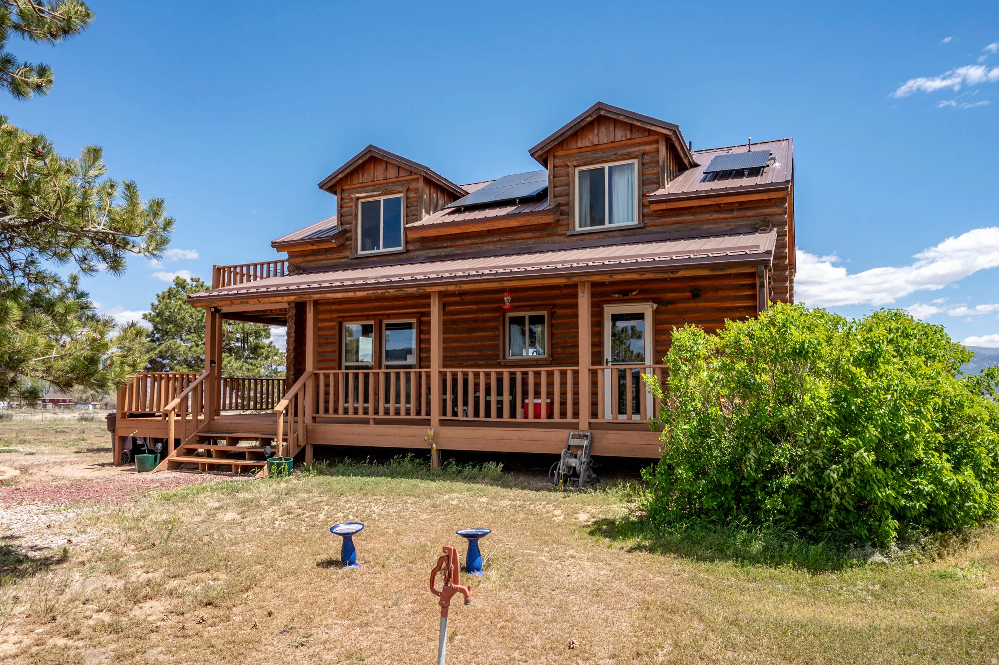 Log home exterior featuring a covered porch, upper-level deck, dormer windows, and a metal roof