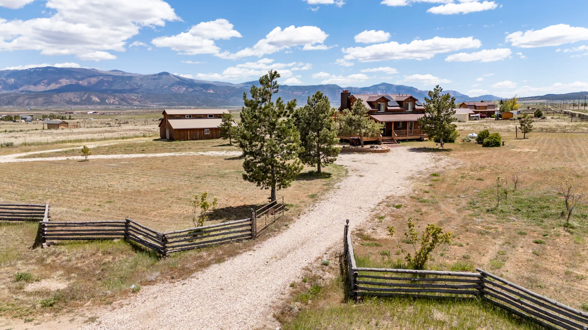 Expansive property featuring a rustic-style residence with a porch, a separate barn structure, and a gravel driveway