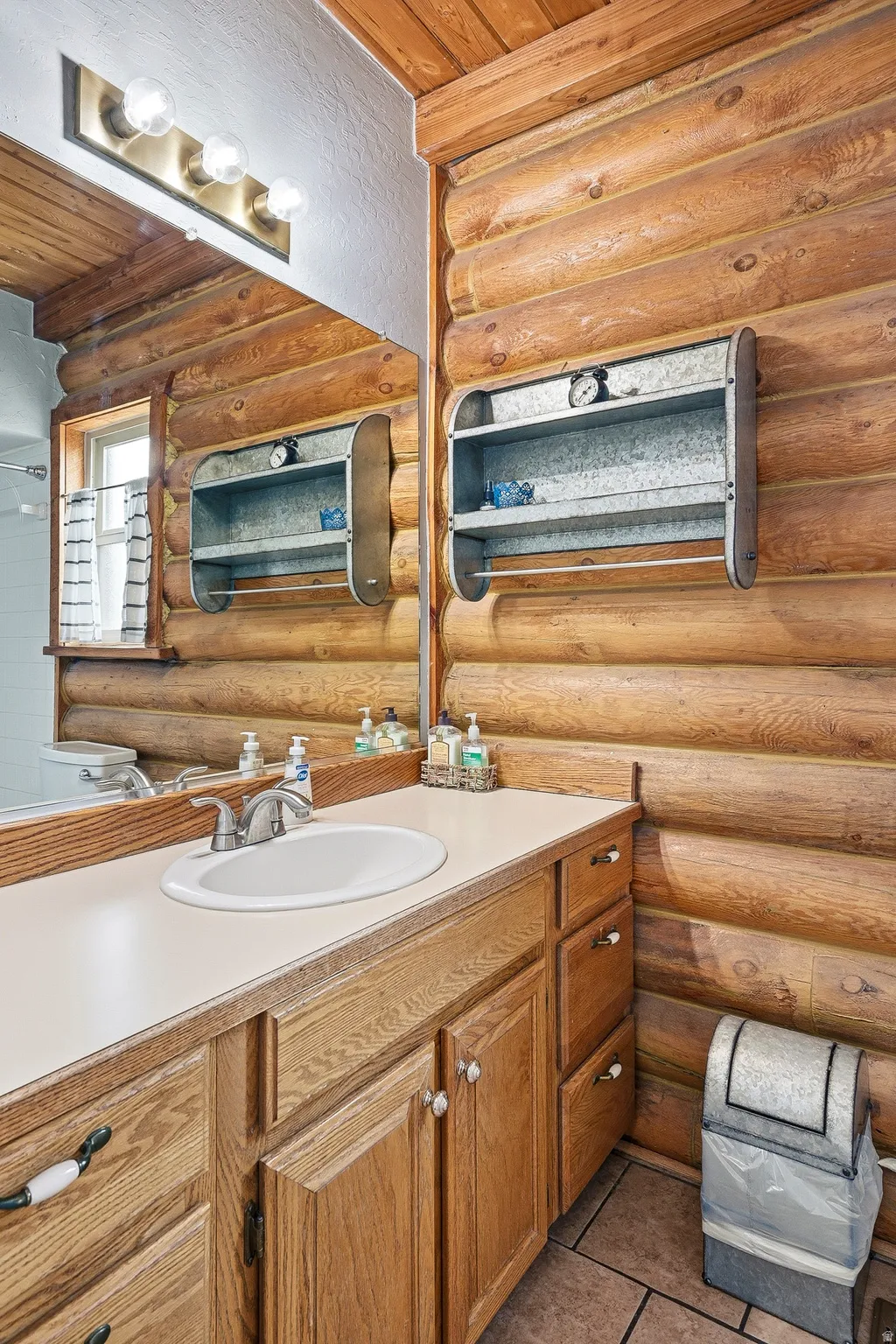 Bathroom vanity with an integrated oval sink, set against log-style walls and tile flooring