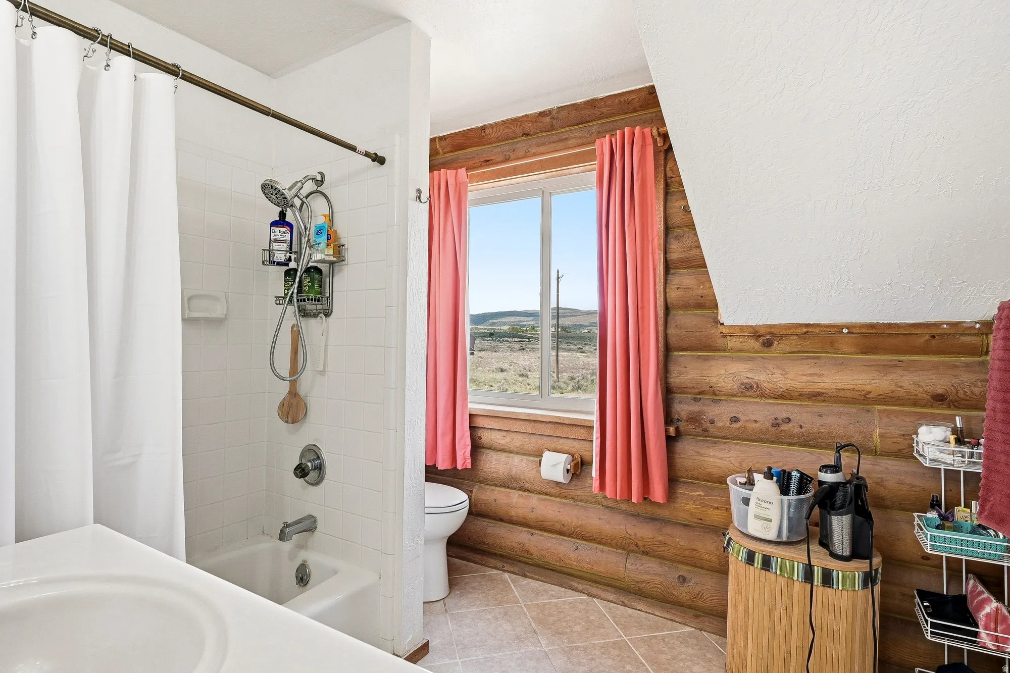 Bathroom featuring a white bathtub and shower combination, white tiled walls, and a window with a rural landscape visible