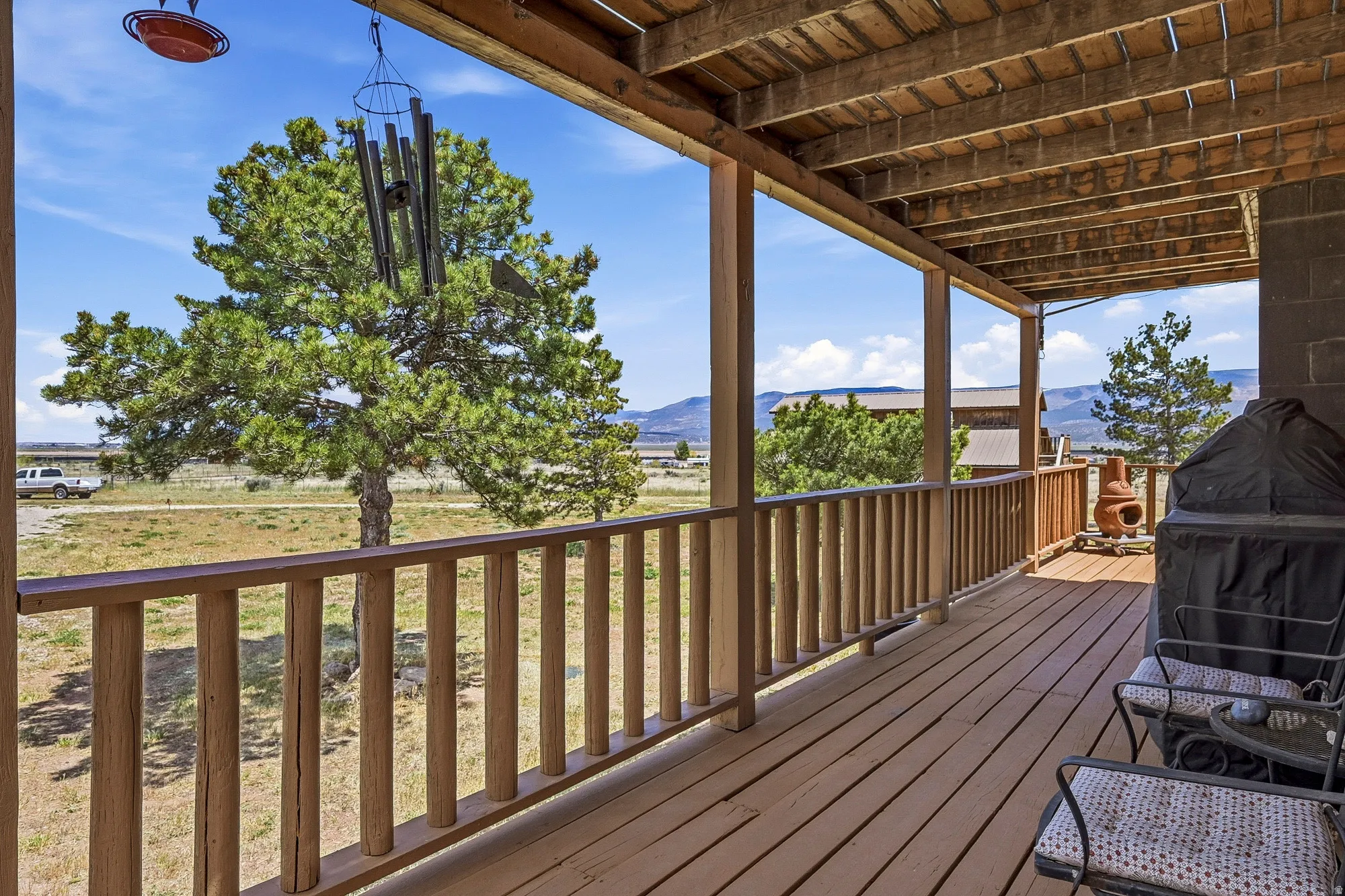 Expansive outdoor deck featuring wood flooring and railings, overhead wood beam ceiling, and mountain scenery