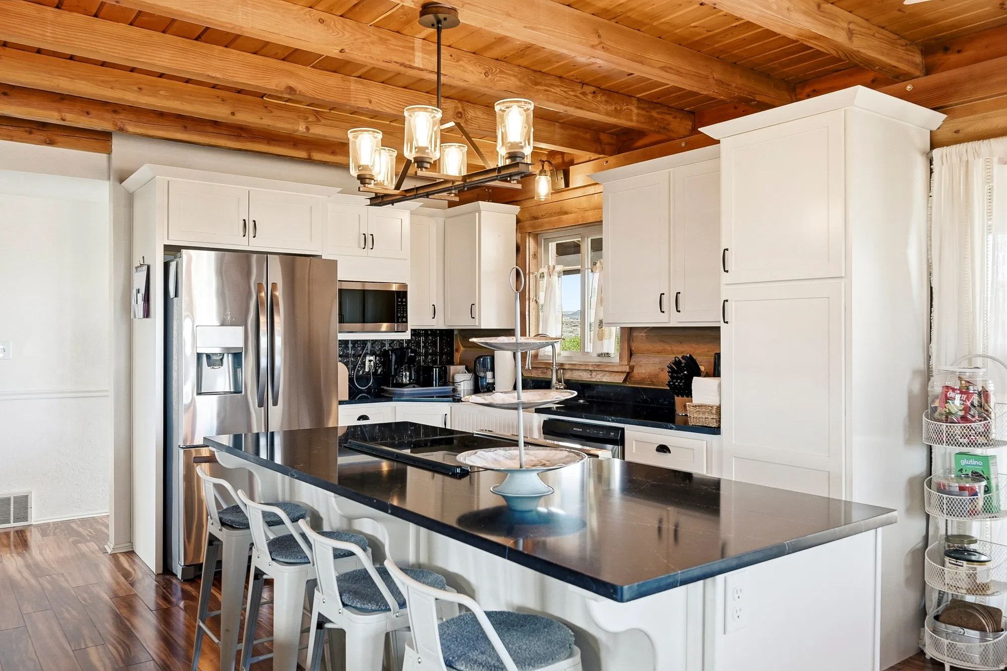 Open-concept kitchen featuring an eat-at island with a dark countertop, white cabinetry with dark hardware, stainless steel appliances, and wood-finish flooring