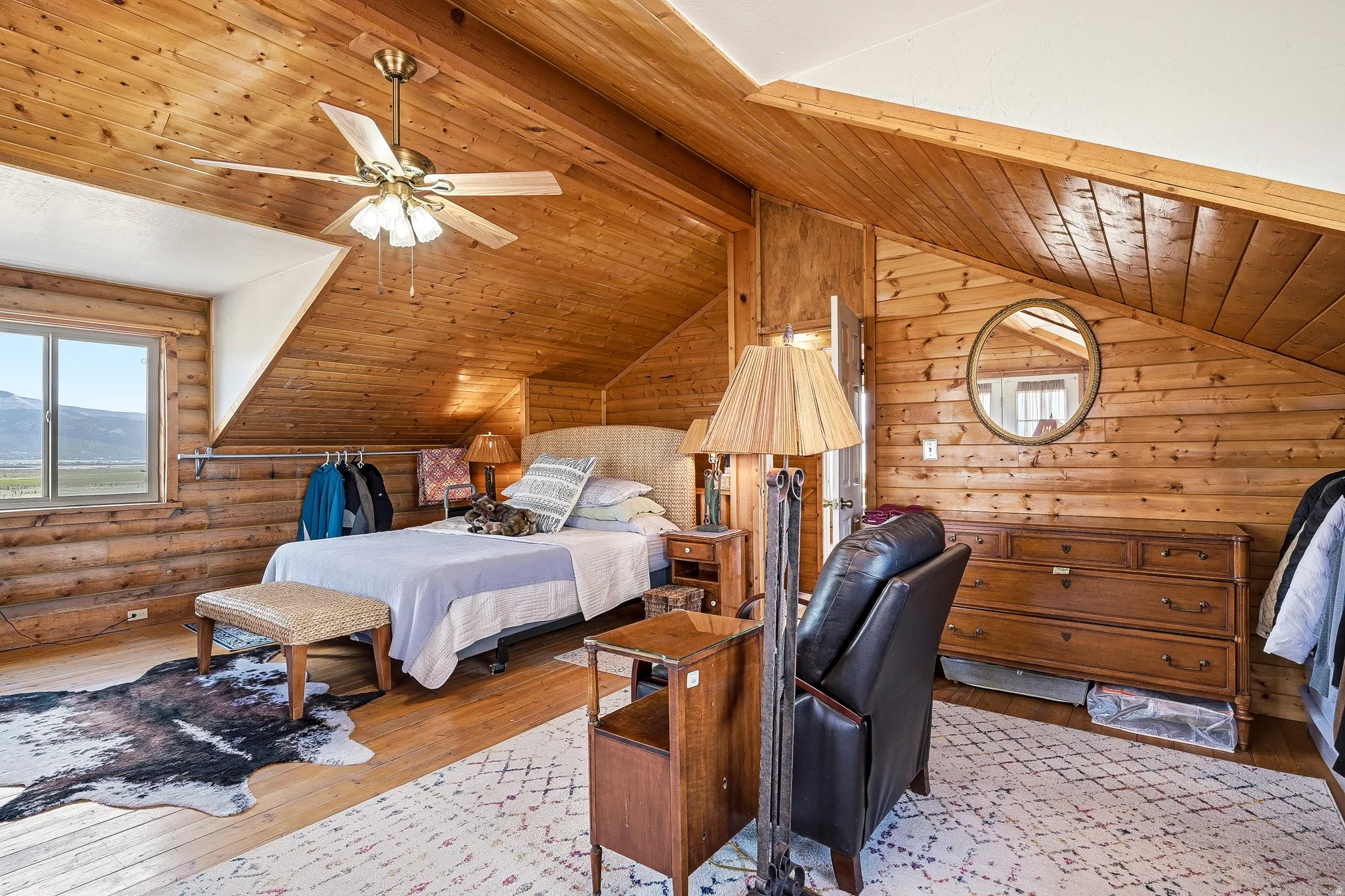 Attic bedroom with extensive wood paneling, sloped wood-paneled ceilings, a window with a landscape vista, and a ceiling fan light fixture