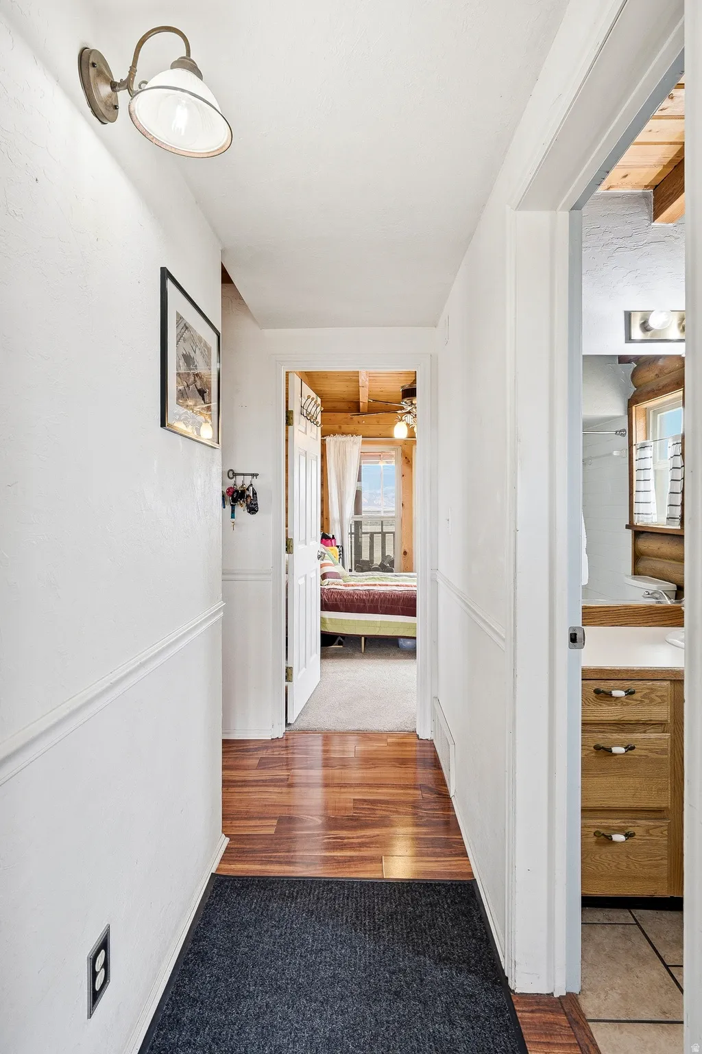 Hallway featuring wood-finish flooring, white painted walls with chair rail molding, and a sconce light fixture