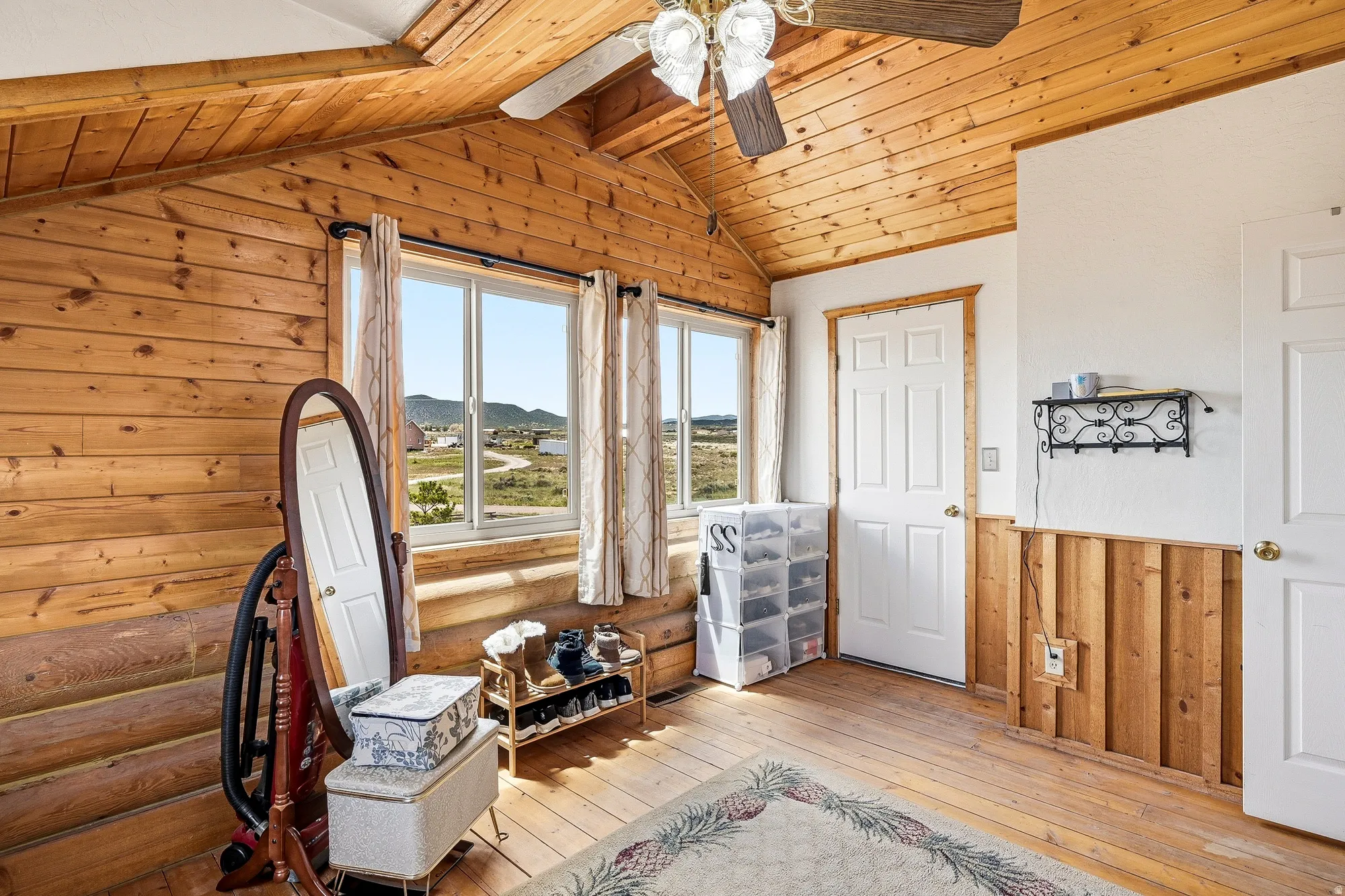 Room featuring wood-plank walls and ceiling, wood-finish flooring, two multi-pane windows, and a ceiling fan with integrated lighting