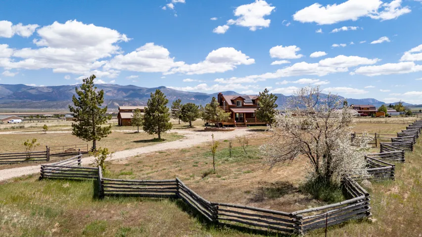 Expansive property featuring a rustic split-rail fence, mature trees, and a gravel driveway