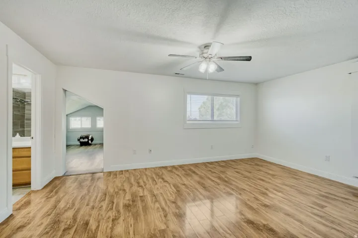 Spacious room featuring wood-finish flooring, a ceiling fan, and a window with blinds