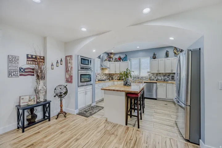 Kitchen featuring a central island with countertop, stainless steel appliances, light-toned cabinetry, and wood-finish flooring