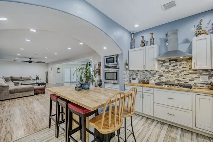 Contemporary kitchen with white cabinetry, wood-finish countertops, a mosaic tile backsplash, and stainless steel appliances