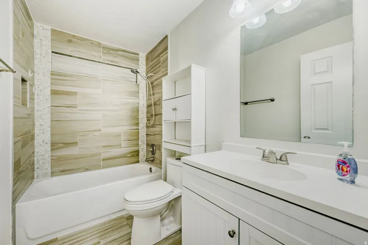 Full bathroom featuring a white porcelain tub, wood-finish tile shower surround, mosaic tile accent, a white vanity with integrated sink, and a large wall-mounted mirror