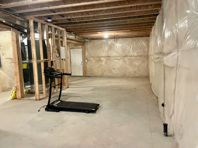 Unfinished basement featuring exposed wood joists, concrete flooring, and partial framing for future customization