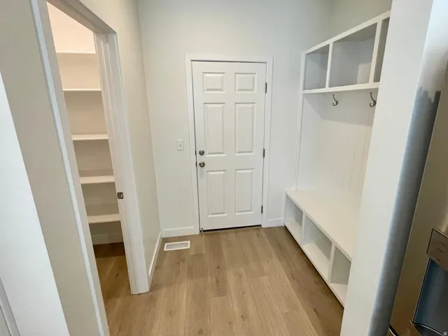 Entryway featuring wood-finish flooring, a white paneled door, and a built-in mudroom bench with open shelving and hooks