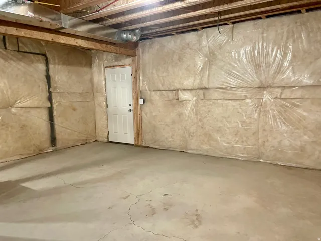 Unfinished basement featuring exposed wood joists, concrete flooring, and a white paneled door