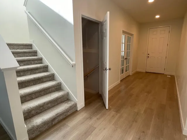 Entryway featuring wood-finish flooring, a carpeted staircase with a white railing, a paneled front door, and French doors leading to an interior space
