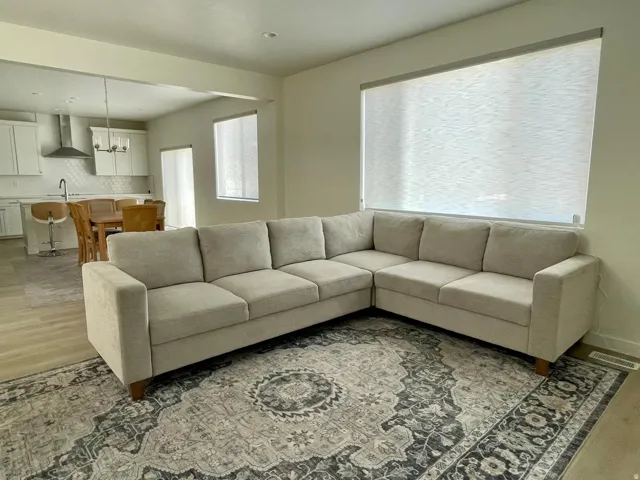 Bright living area with light wood-finish flooring and a large window featuring roller shades
