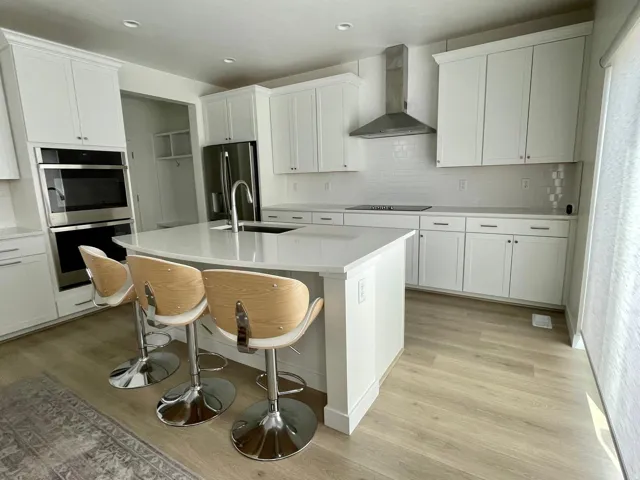 Spacious kitchen featuring a large central island with seating, white shaker cabinetry, stainless steel appliances, and wood-finish flooring