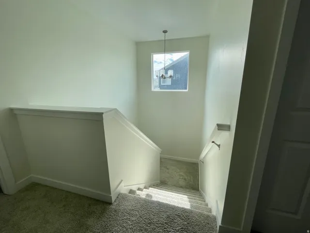 Carpeted staircase featuring a rectangular window, a suspended chandelier, a wall-mounted handrail, and white baseboards