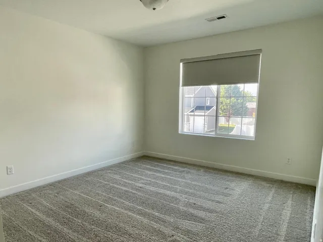 Bright room featuring a window with roller shade, neutral wall paint, and patterned gray carpeting