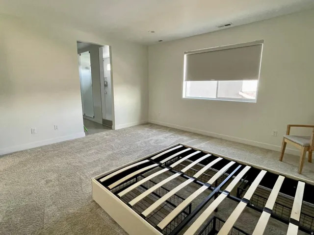 Spacious room with light-colored carpeting, white baseboards, and a large window featuring a roll-down shade