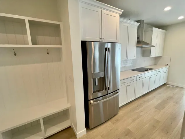 Kitchen and mudroom area featuring stainless steel appliances, white cabinetry, a built-in bench with storage, wood-finish flooring, and a subway tile backsplash