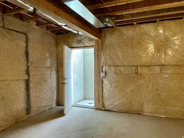 Unfinished basement space featuring exposed wood joists and subflooring, concrete flooring, and insulated walls with a vapor barrier