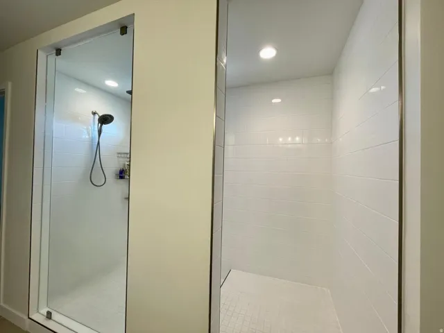 Dual walk-in showers featuring subway tile surrounds, recessed lighting, glass enclosures, and matte black fixtures