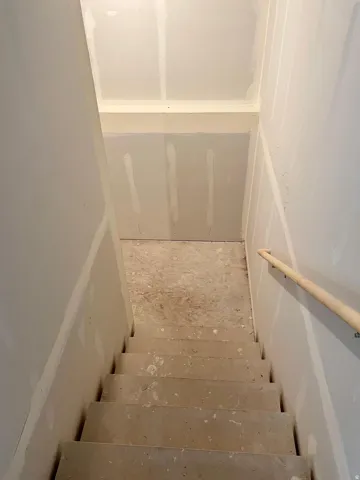 Concrete staircase with a light wood-finish handrail, surrounded by drywall-finished walls