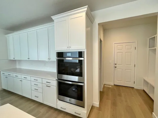 Modern kitchen featuring white shaker cabinetry, stainless steel double wall ovens, light-toned countertops, subway tile backsplash, and wood-finish flooring