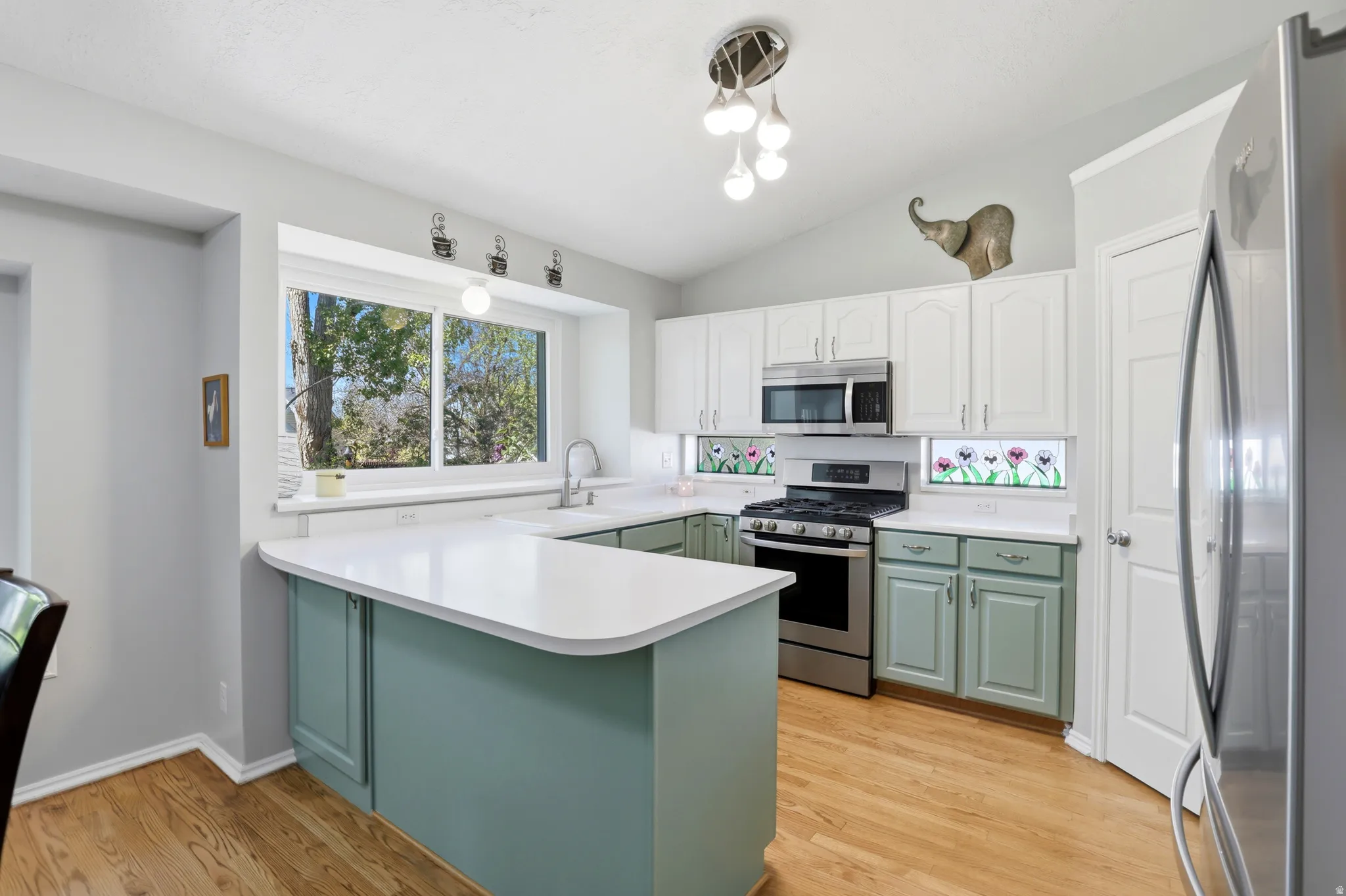 Kitchen featuring a peninsula island with counter seating, stainless steel appliances, white upper cabinetry, and light green lower cabinetry