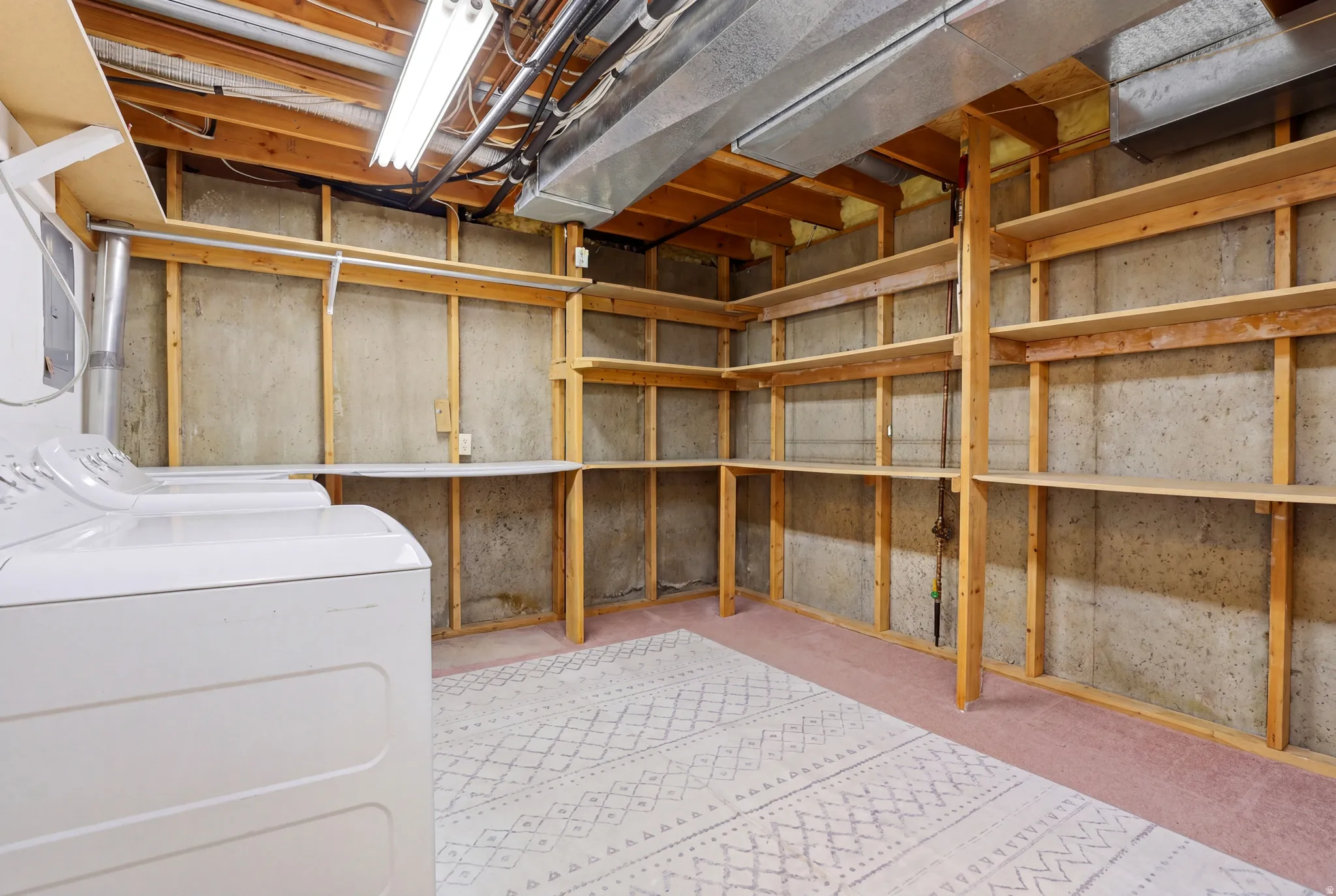 Utility room featuring a washer, dryer, built-in shelving, concrete walls, and overhead lighting