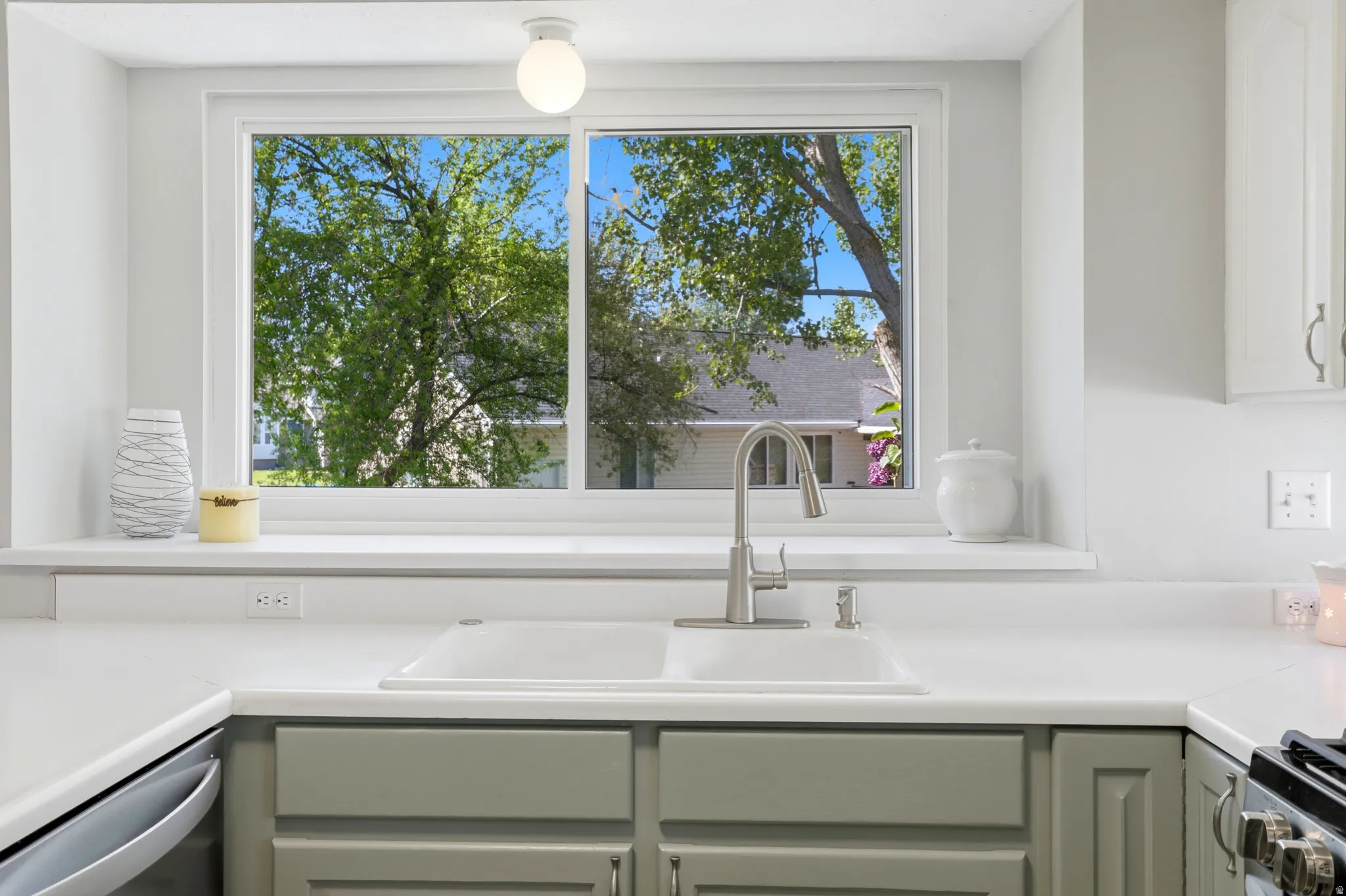 Kitchen featuring a double basin sink with a chrome faucet, light grey cabinetry, white countertops, and a large window overlooking mature trees