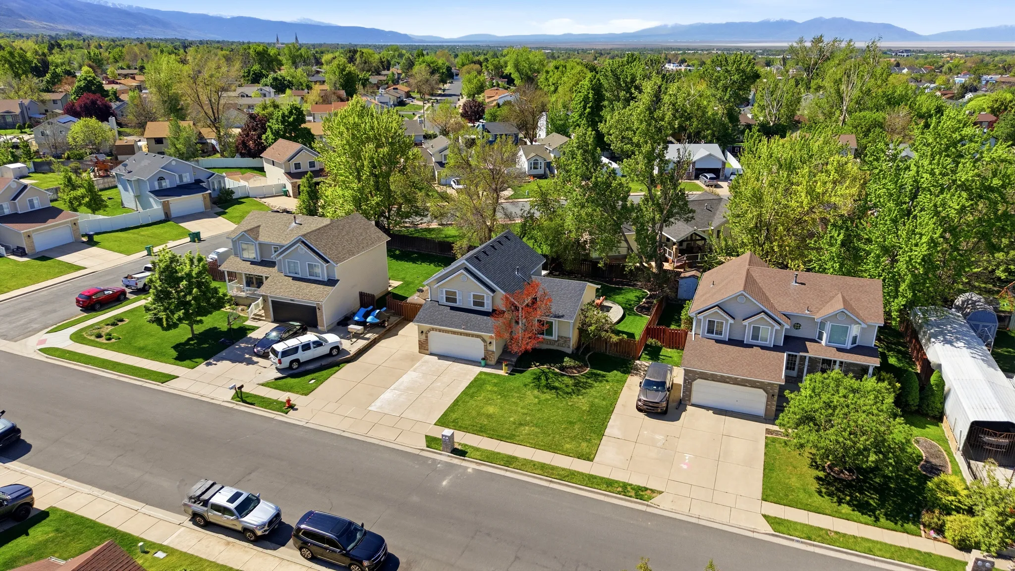 Suburban street with established homes, mature trees, and mountain backdrop