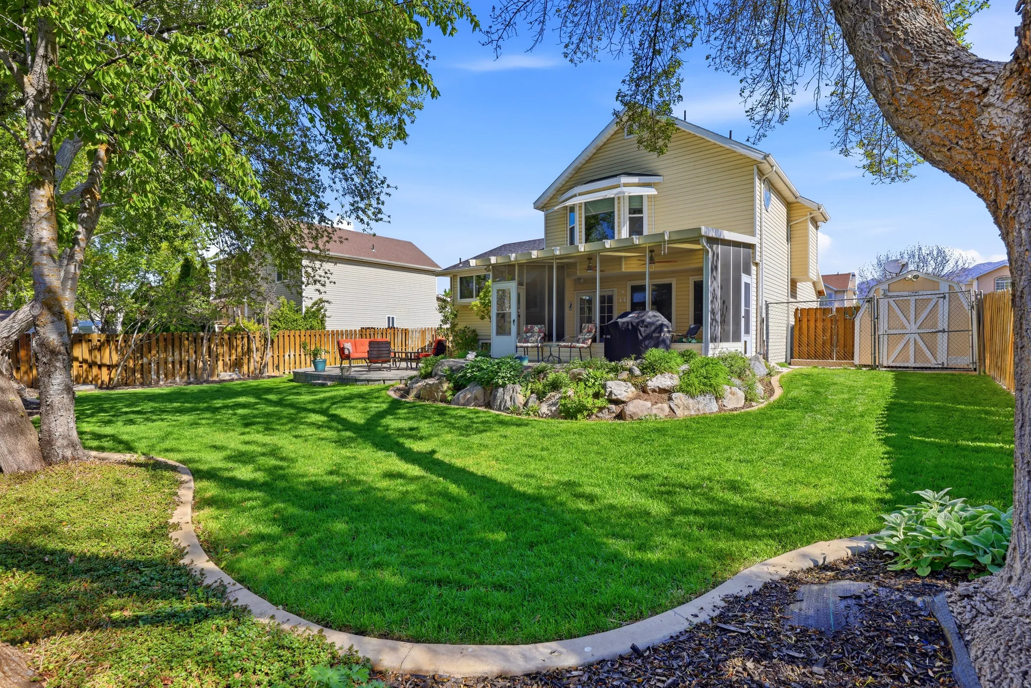 Expansive backyard featuring a manicured lawn, a concrete patio, and a screened porch