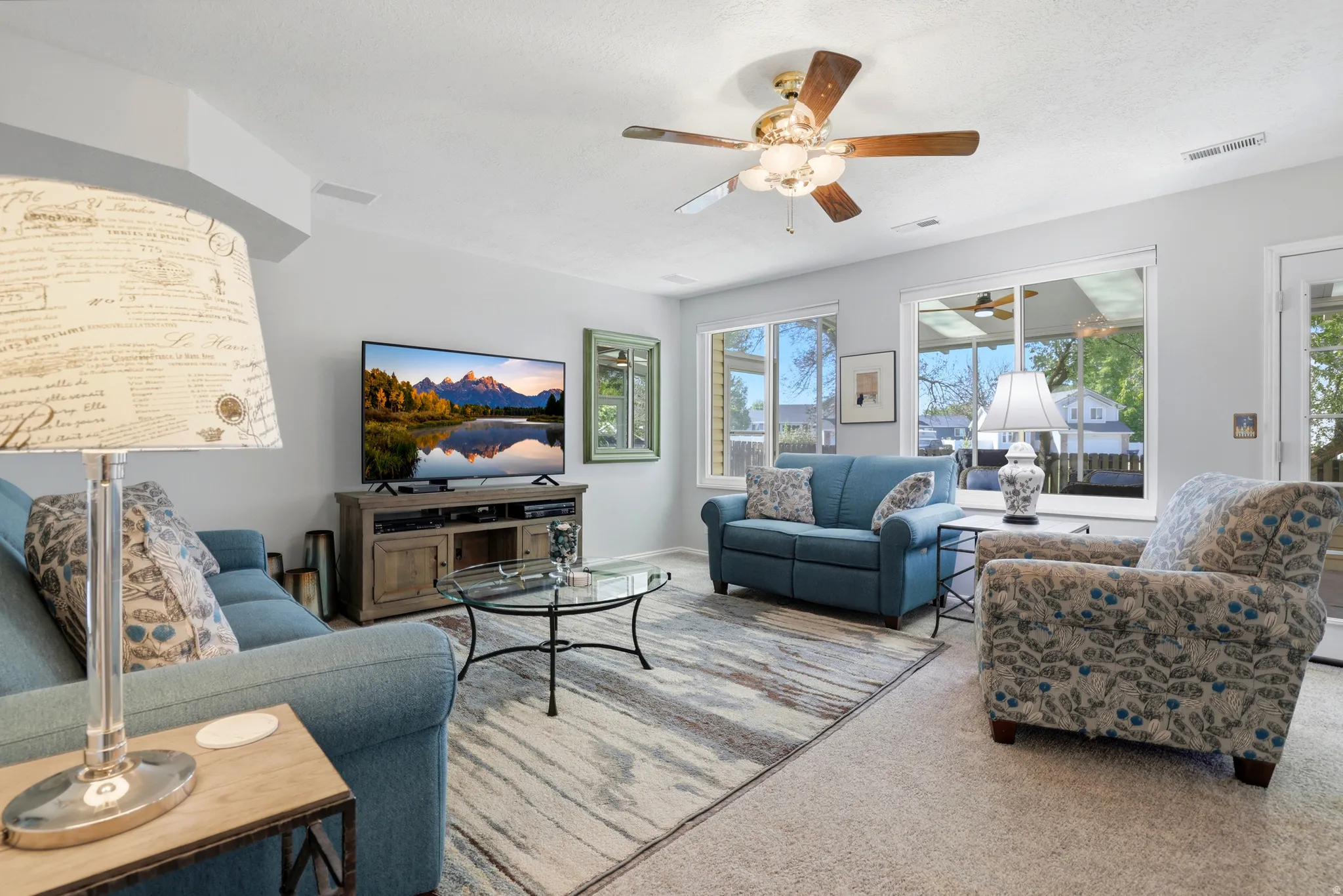 Spacious living area featuring light gray walls, carpet flooring, and a ceiling fan with integrated lighting
